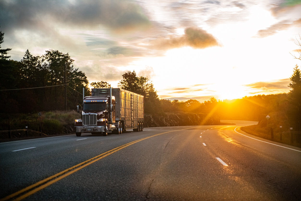 Semi-truck driving down a road at sundown