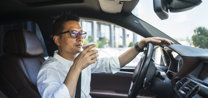 A man drives with one hand while drinking a cup of coffee