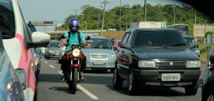 A man on a motorcycle is lane splitting while there is traffic