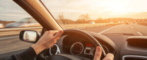 A person driving on a road with the sun facing them